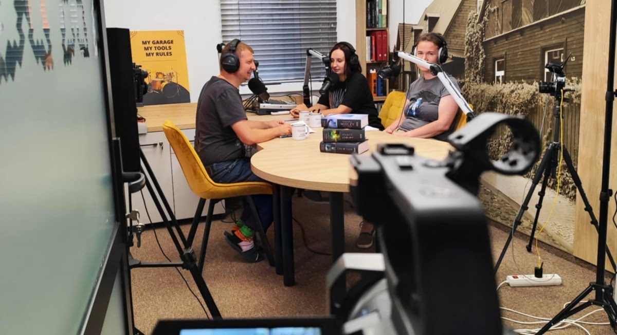 Trzy osoby siedzące przy stole w trakcie nagrywania podcastu