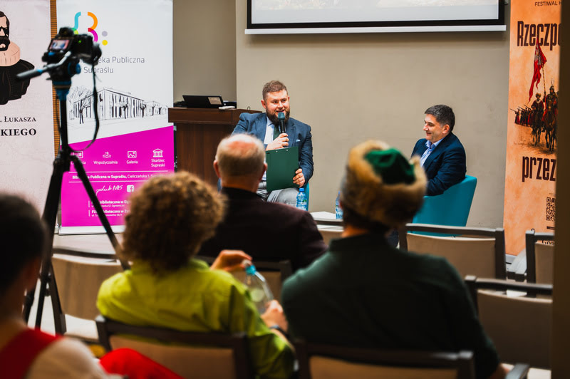 Rozmowa z prof. Guzowskim - prowadzący i profesor siedzą, na pierwszym plane widoczna publiczność
